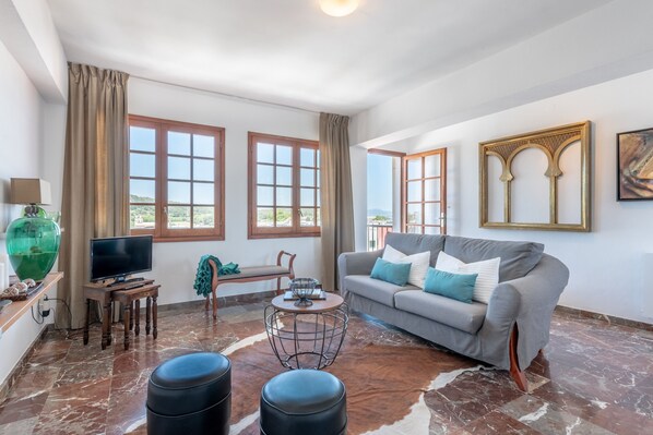 A living room with a sofa, a television, a coffee table, and a view of the outdoors through large windows.