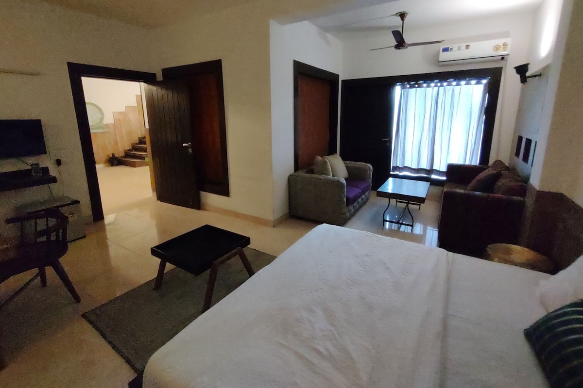 A hotel room with a bed, a sofa, a small table, a TV, and a ceiling fan.