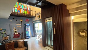 A lobby with a checkered sofa, a round table, a vending machine, and a staircase leading to an upper level. - Aakritii Hotels (Gurugram)