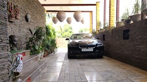 A car parked in a covered driveway with stone walls and potted plants. - Aakritii Hotels (Gurugram)