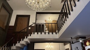 A grand staircase with a chandelier, a fire exit sign, and a unique wall art piece. - Aakritii Hotels (Gurugram)