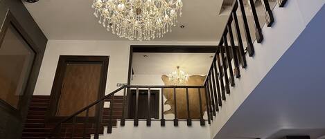 A grand staircase with a chandelier, a fire exit sign, and a unique wall art piece.