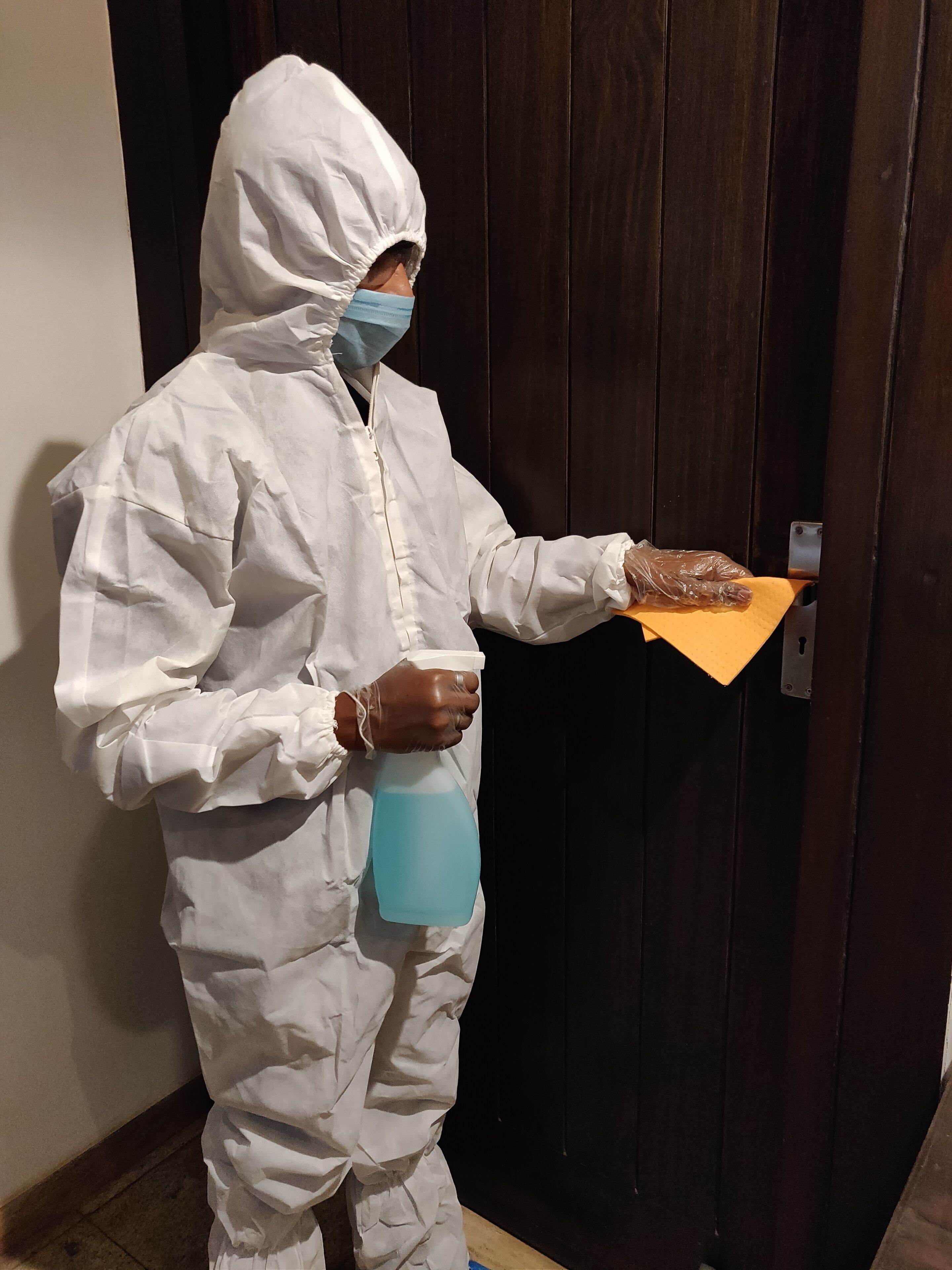 A person in a white protective suit holding a spray bottle and a tray with a brown object.