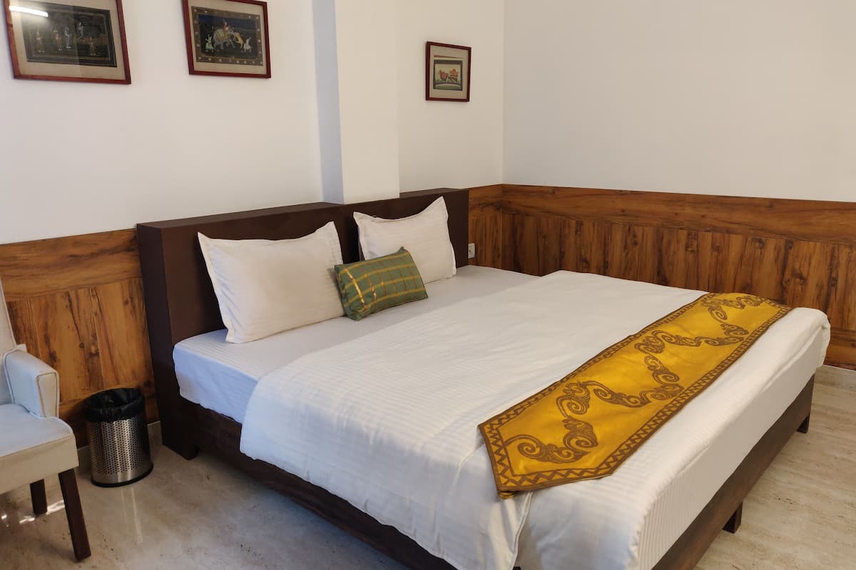 A neatly made bed with white bedding and a yellow decorative throw. There are two pillows, one green and one white. The room has wooden paneling on the walls and a small trash can next to the bed.
