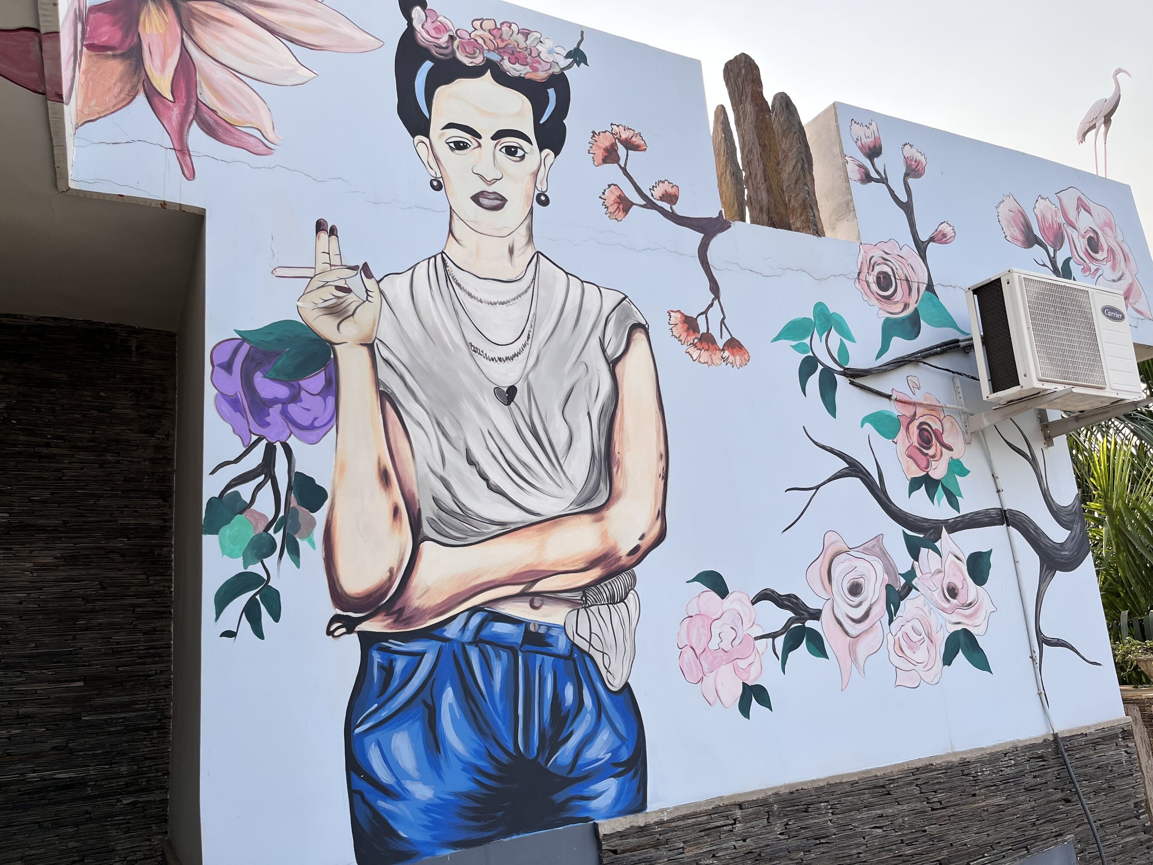 A mural of a person with flowers in their hair, a bird, and a tree with pink flowers.