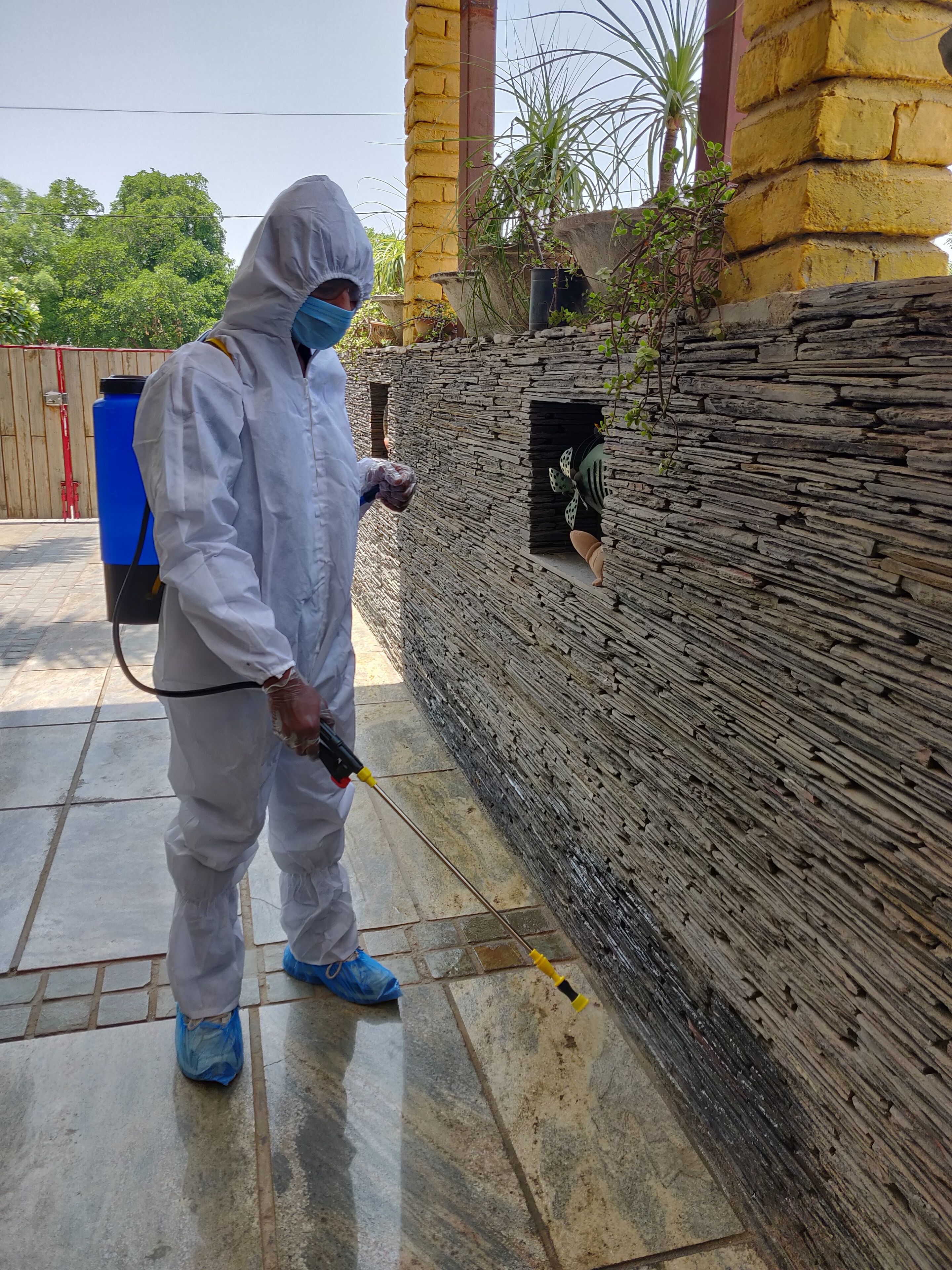 Una persona con equipo de protección usando un atomizador sobre una pared de piedra.