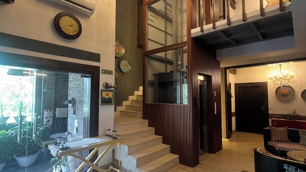 A spacious living area with a staircase, a chandelier, and a view of the outdoors. - Aakritii Hotels (Gurugram)