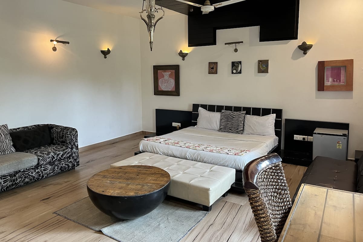 A modern bedroom with a bed, two sofas, a round coffee table, and a ceiling fan.