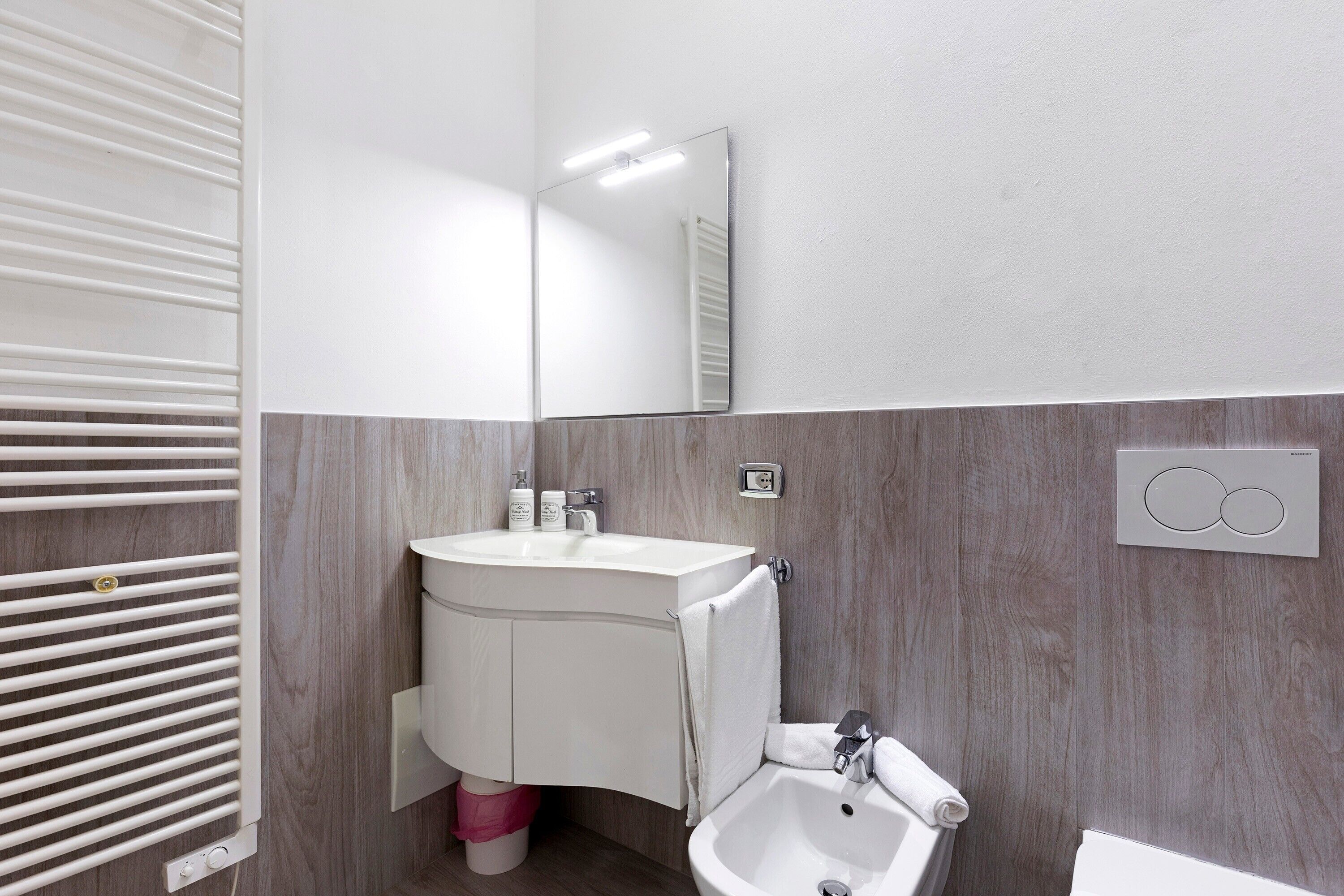 A modern bathroom with a white sink, mirror, and built-in heater.