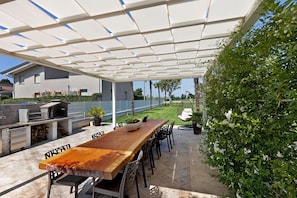 Un patio exterior con una mesa y sillas de madera, una parrilla y una pérgola.