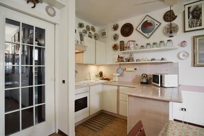 A kitchen with white cabinets, a microwave, a kettle, and various decorative plates on the wall.