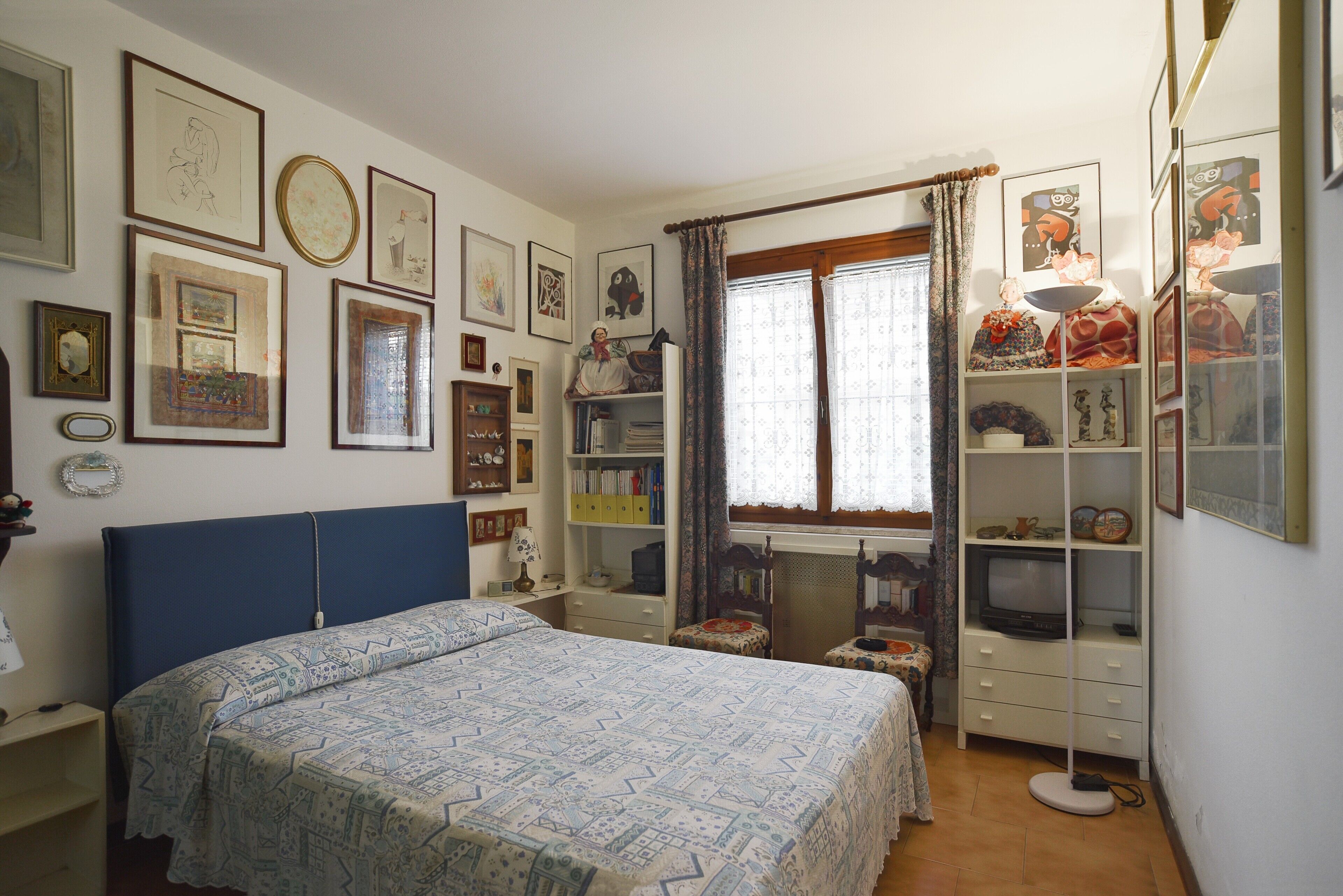Una camera da letto con un letto, una TV, uno scaffale con oggetti decorativi e diverse foto incorniciate appese al muro.