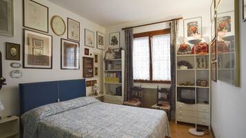 Una camera da letto con un letto, una TV, uno scaffale con oggetti decorativi e diverse foto incorniciate appese al muro.