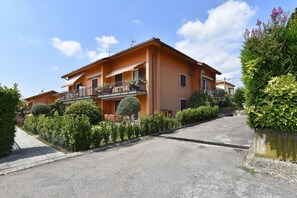A two-story building with a balcony, a driveway, and a well-maintained garden.