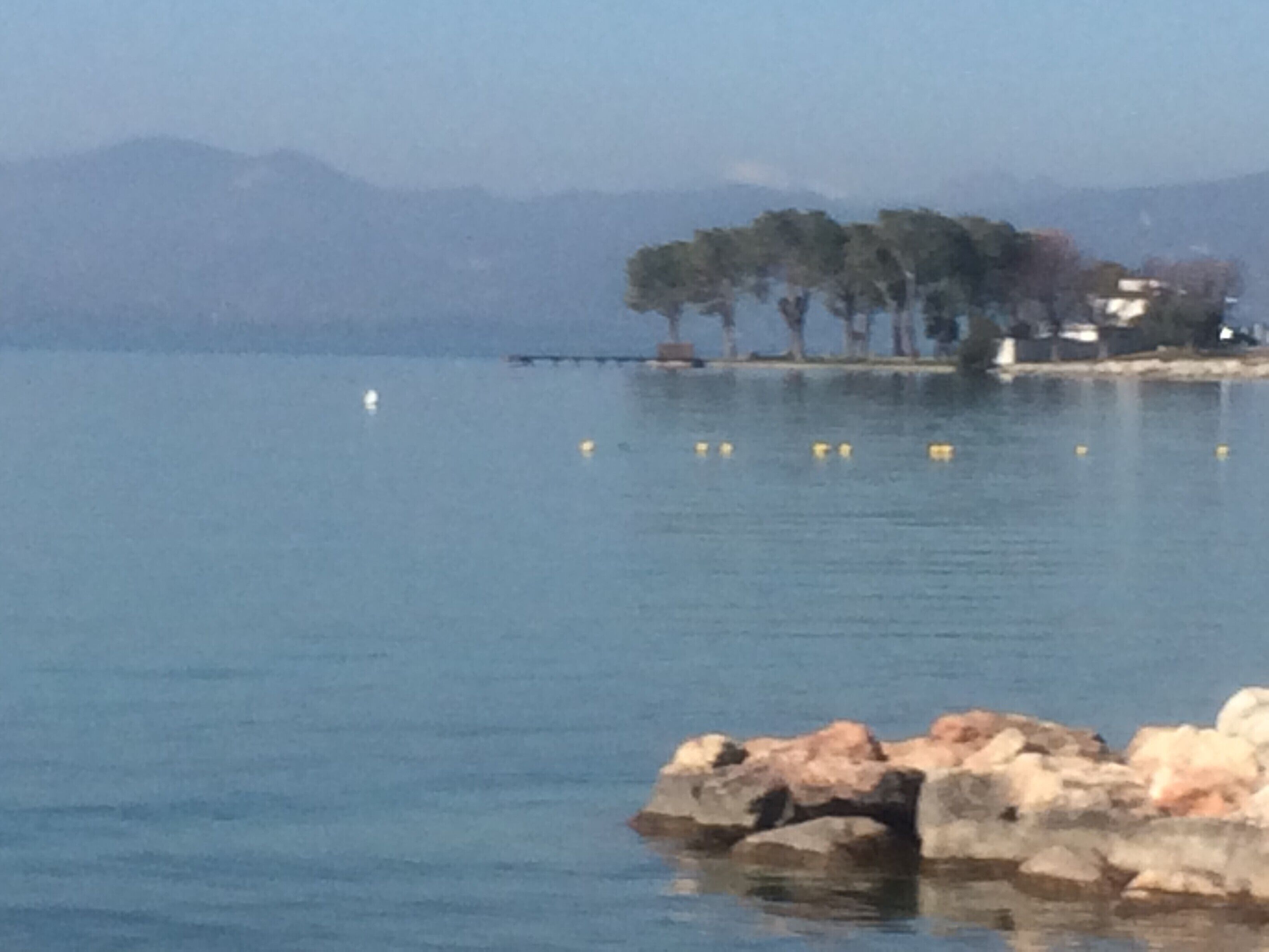 A calm lake with a rocky shoreline and trees in the background.