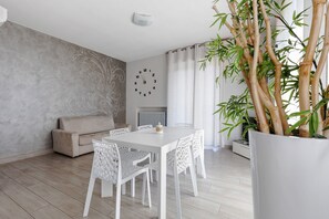 A modern living room with a dining area, a sofa, a clock, and a large bamboo plant.