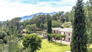 Eine Villa mit gepflegtem Rasen, einem Kiesweg und Blick auf den umliegenden Wald und die Berge.