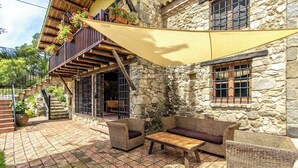 Ein Steinhaus mit Balkon, Sitzbereich im Freien und einer großen Sonnensegel.