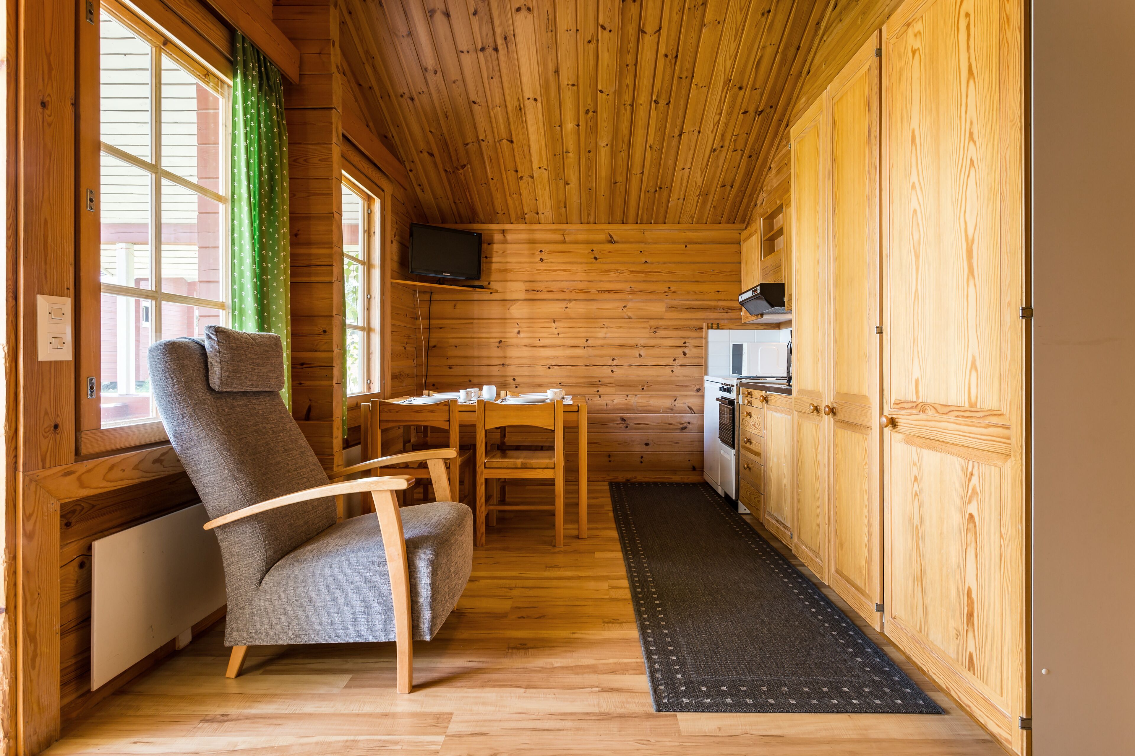 Interior de una cabaña de madera con comedor, sofá, televisor y cocina.