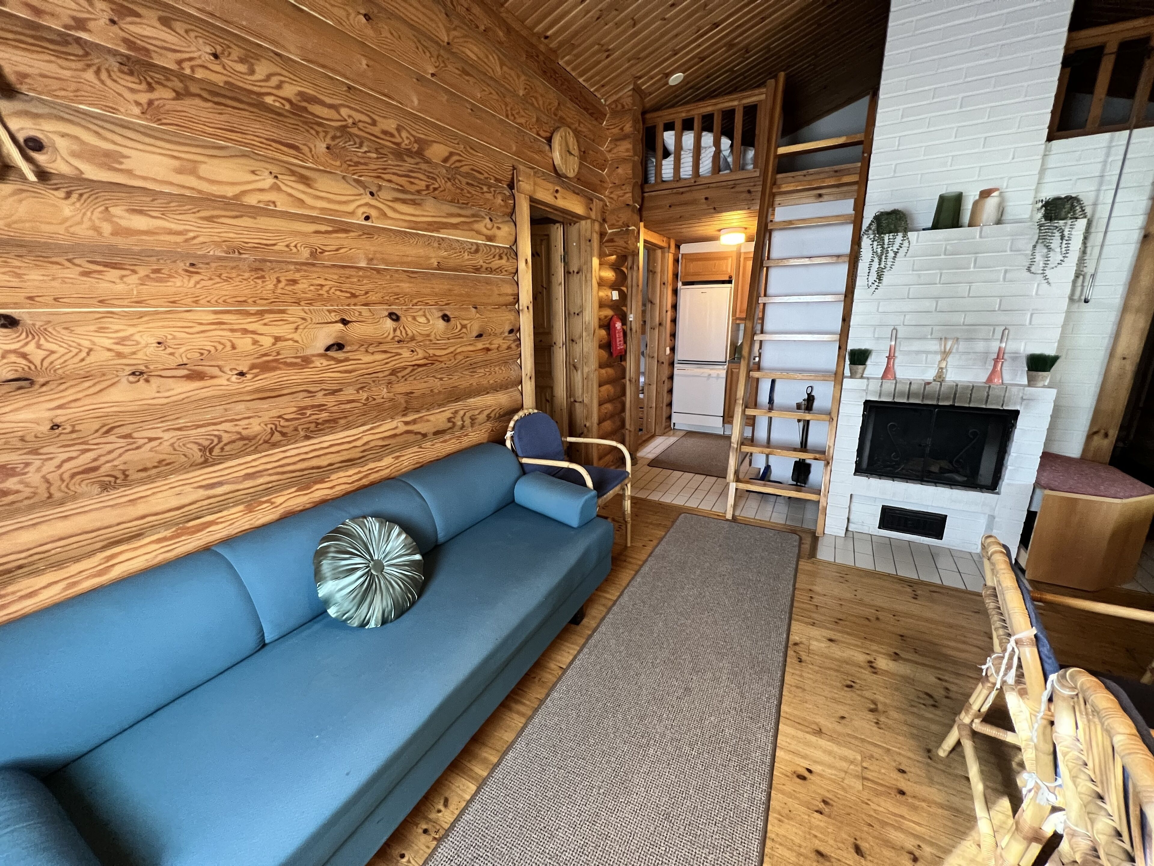 Interior de una cabaña de troncos con un sofá azul, una chimenea y una escalera de madera.