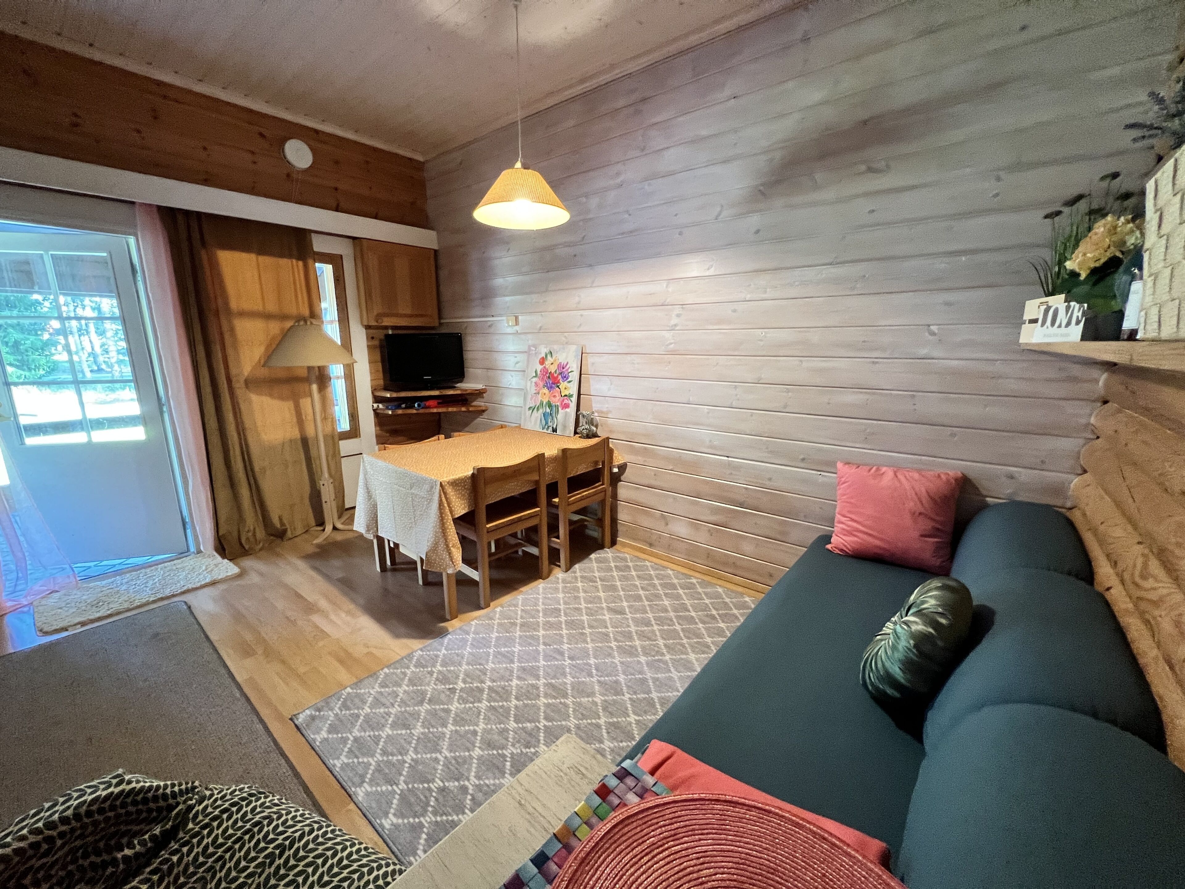 Ein gemütliches Blockhaushaus-Interieur mit Holzausstattung, einer Couch, einem Esstisch und einem Fernseher.