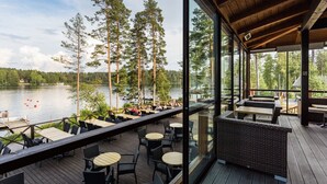 A deck with outdoor seating overlooking a lake, surrounded by tall trees. - Punkaharju Resort (Savonlinna)
