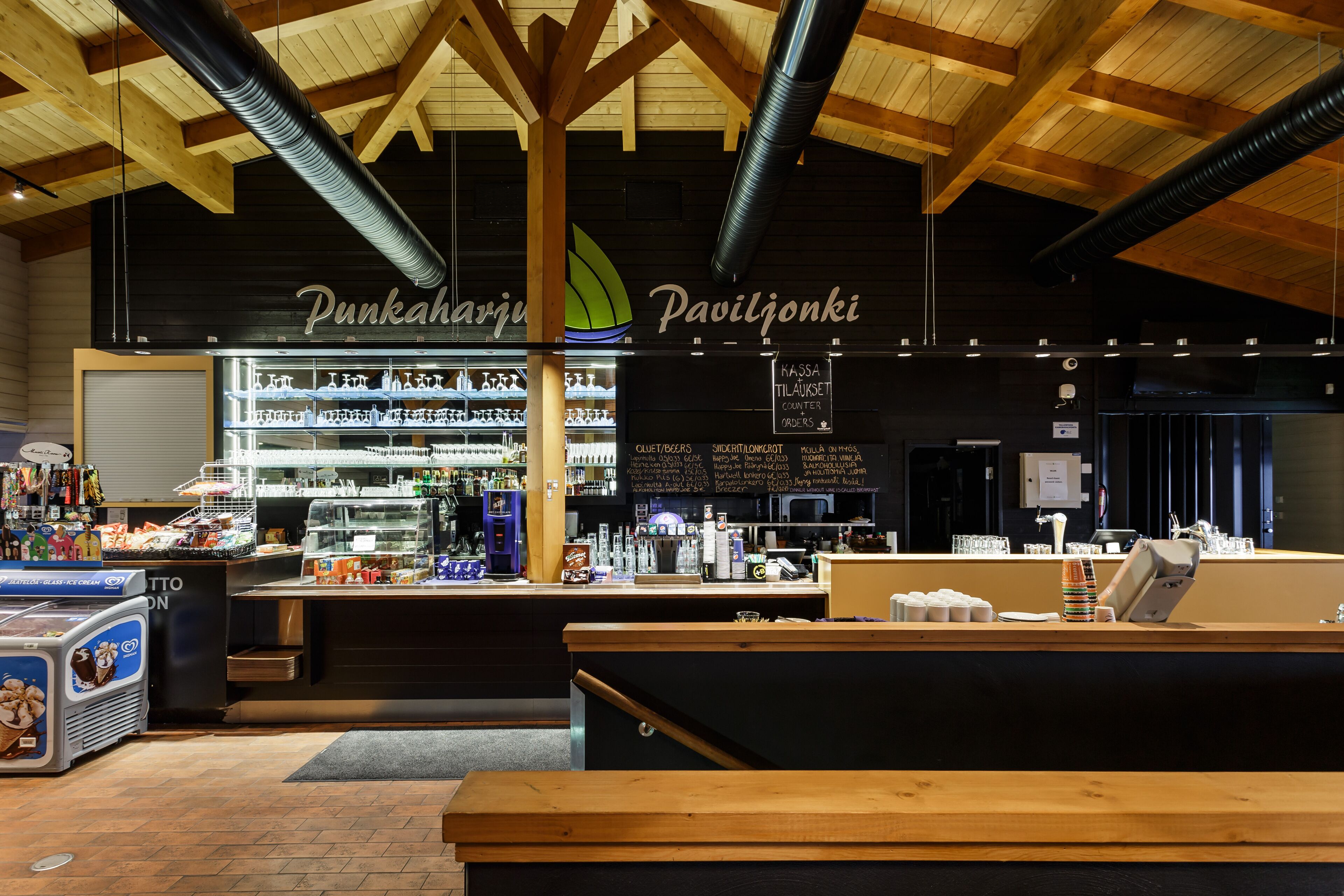 Een restaurant interieur met een houten plafond, een toonbank met een menu en een koelvitrine.
