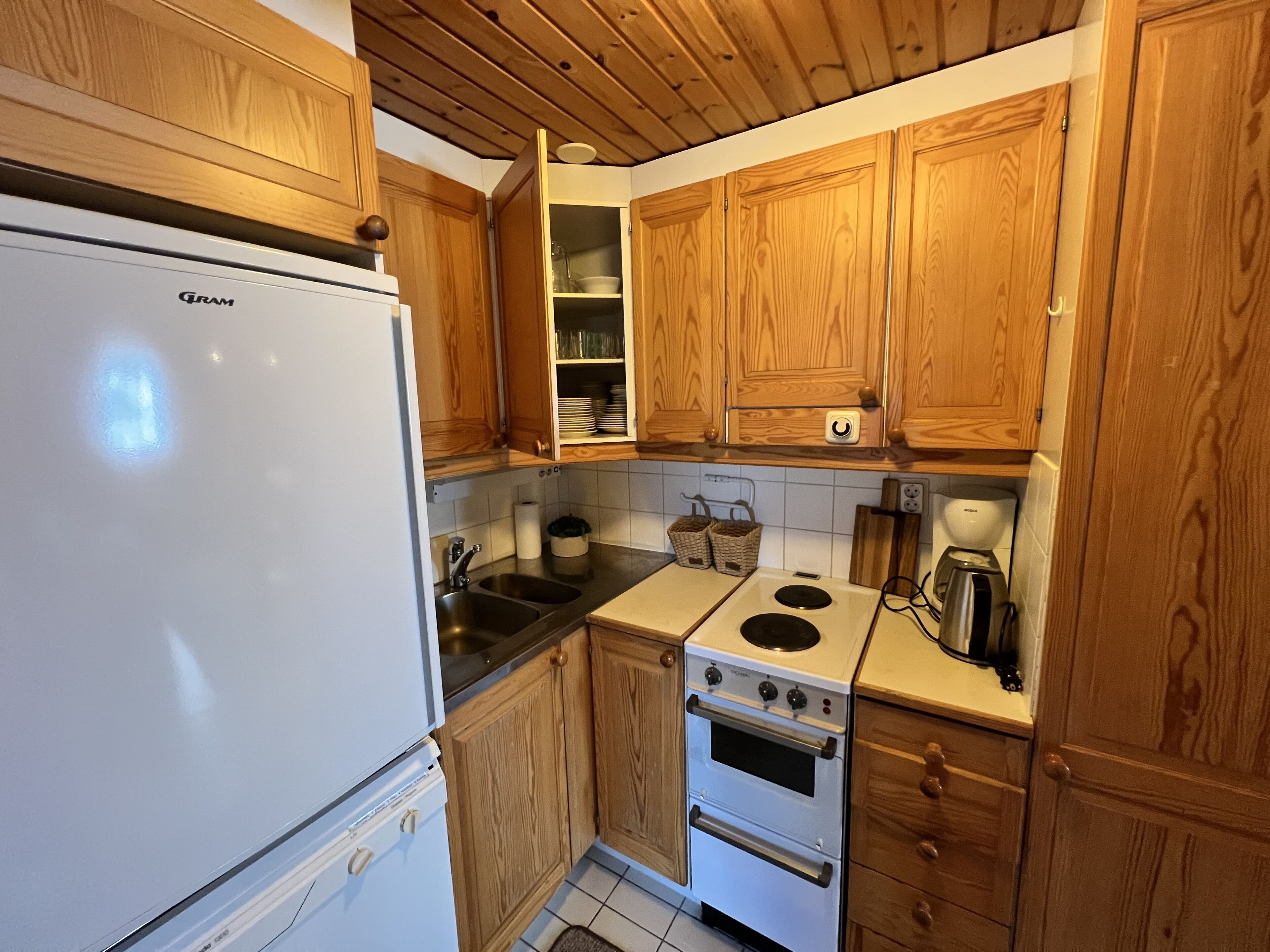 A compact kitchen with wooden cabinets, a white refrigerator, a stove, and a sink.
