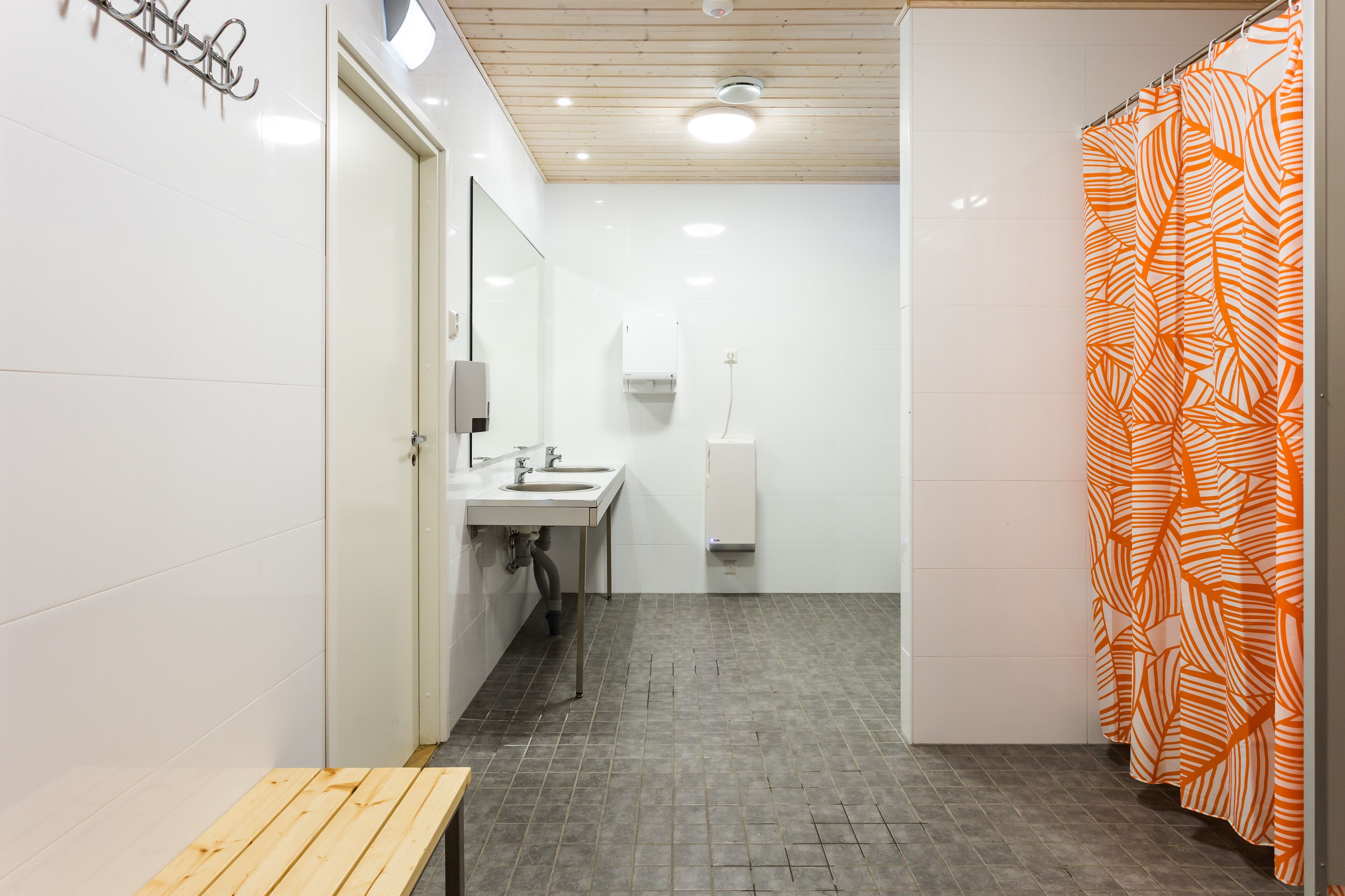 Une salle de bain avec un banc en bois, un lavabo, un miroir et un rideau de douche orné d’un motif de feuilles.
