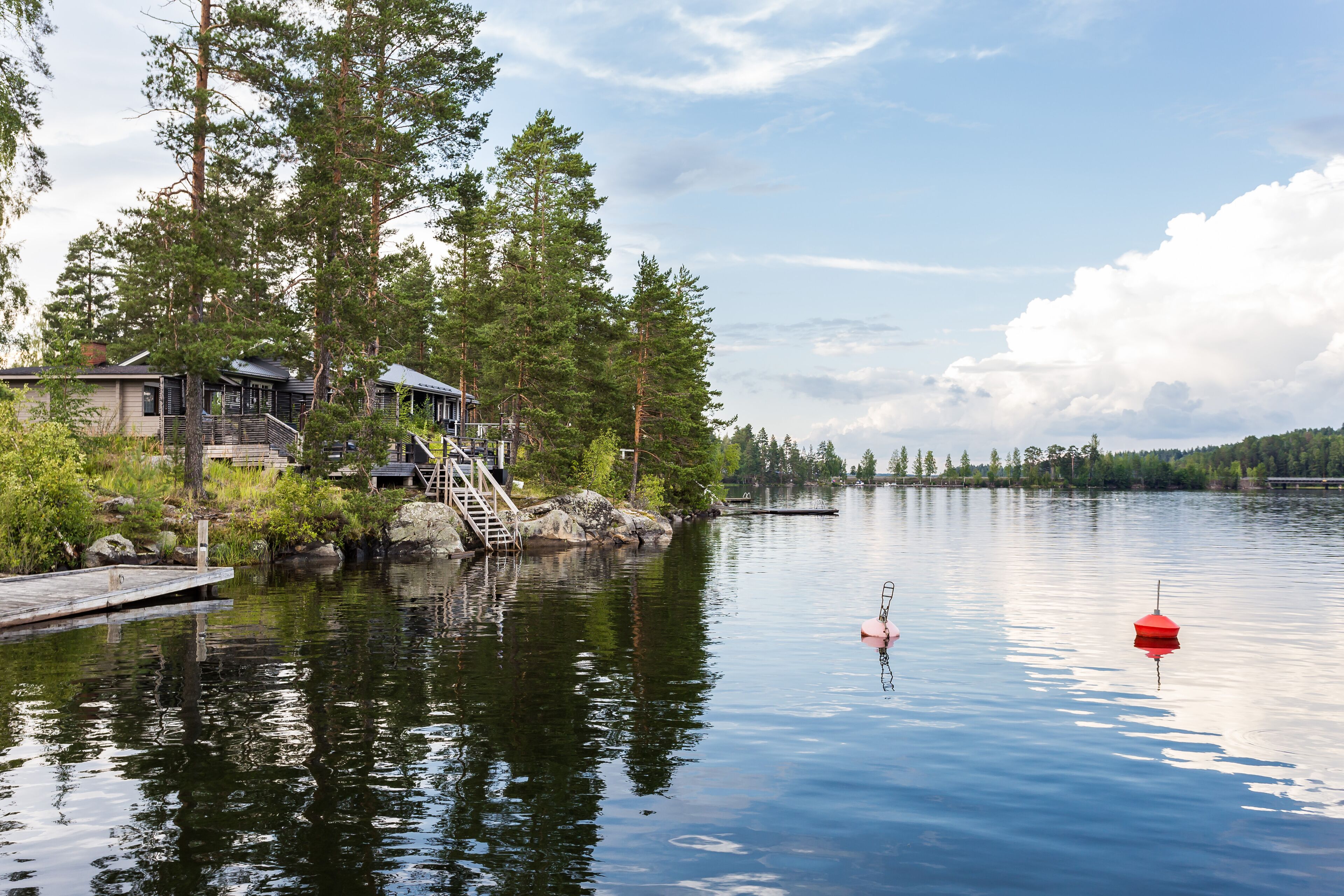A lakeside cabin with a dock, surrounded by tall trees and calm water.
