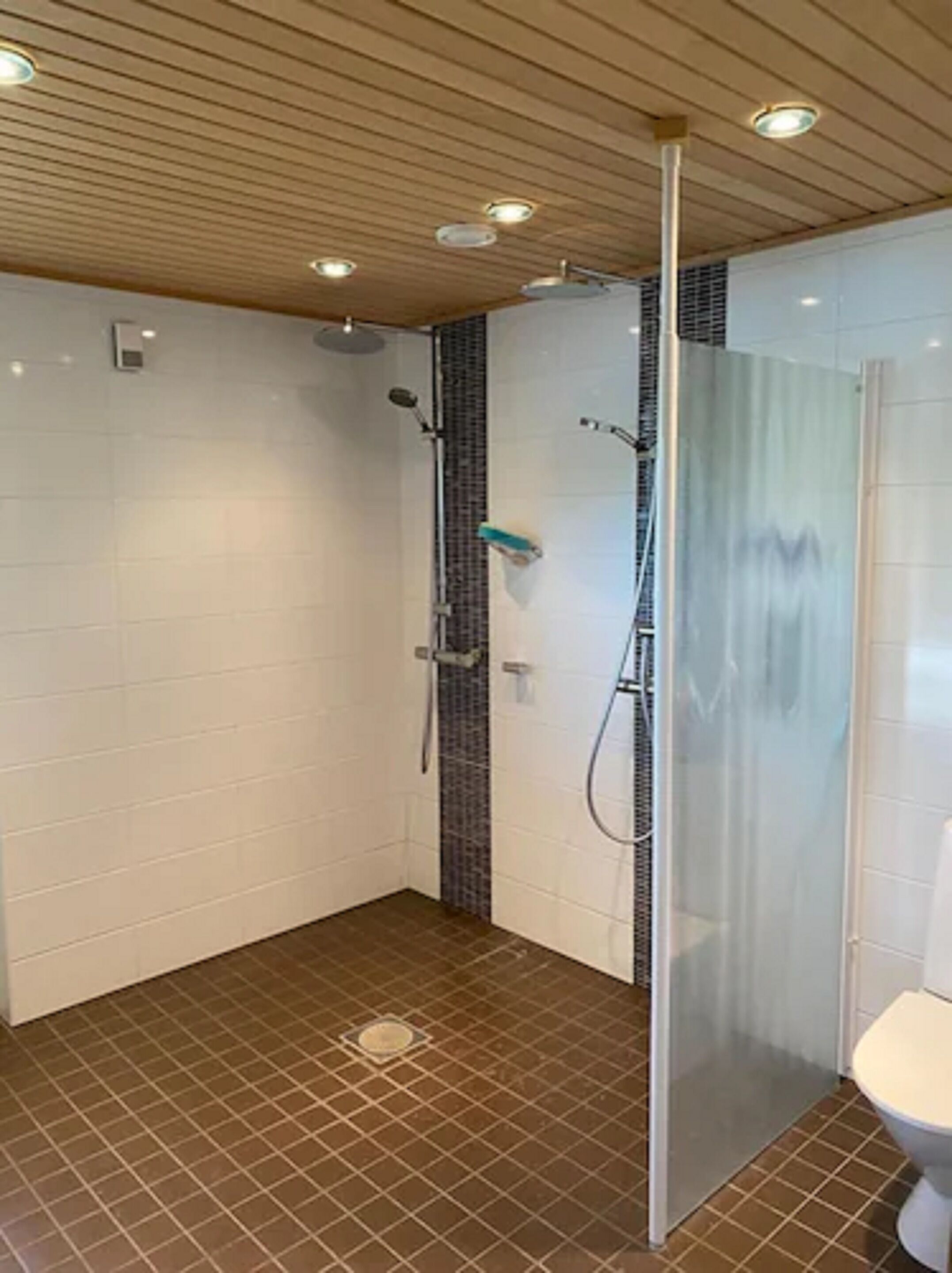 A shower area with a glass partition, tiled walls, and a brown-tiled floor.