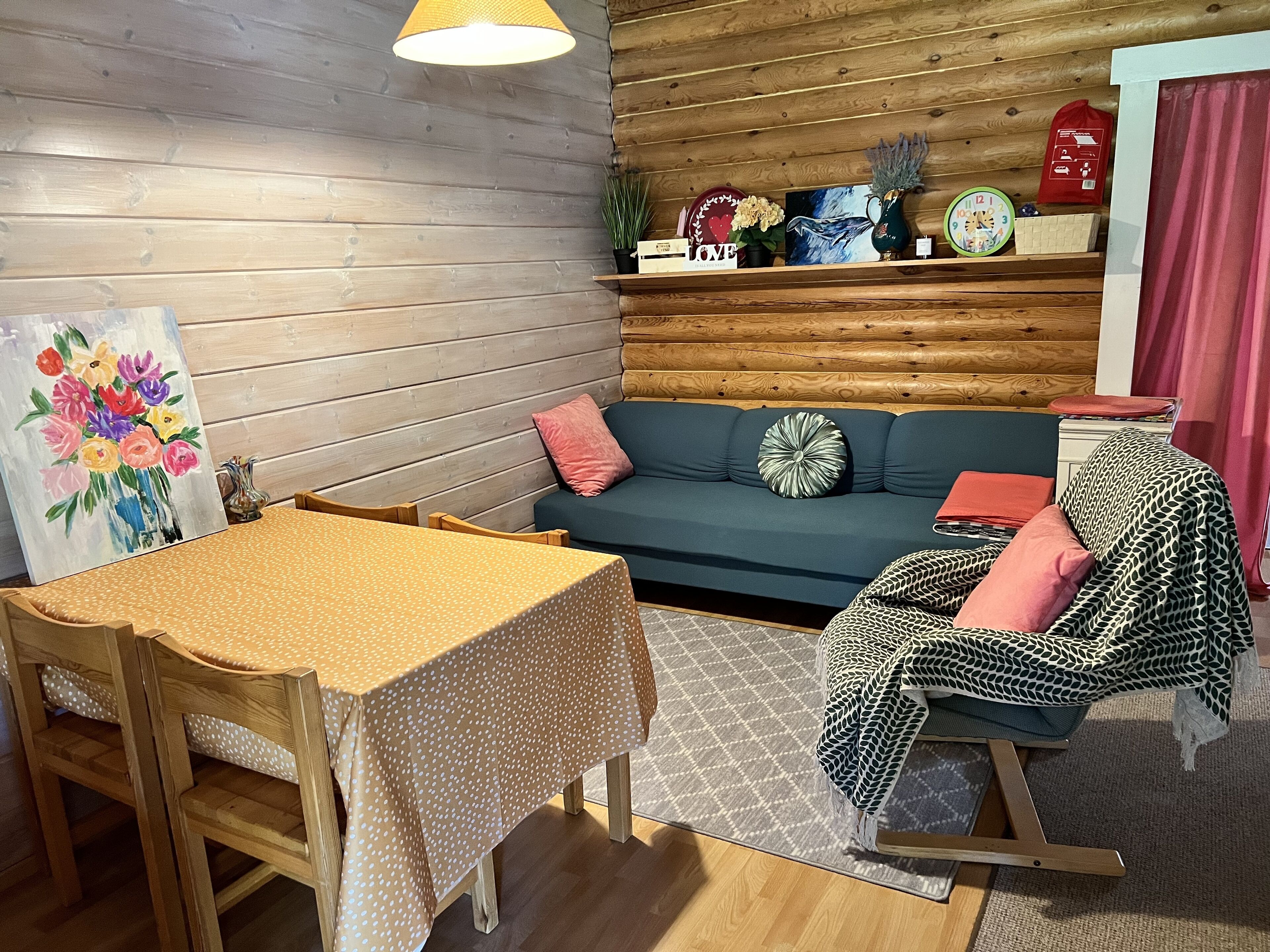 A cozy room with a wooden wall, a sofa, a dining table with a polka-dotted tablecloth, and a rocking chair.