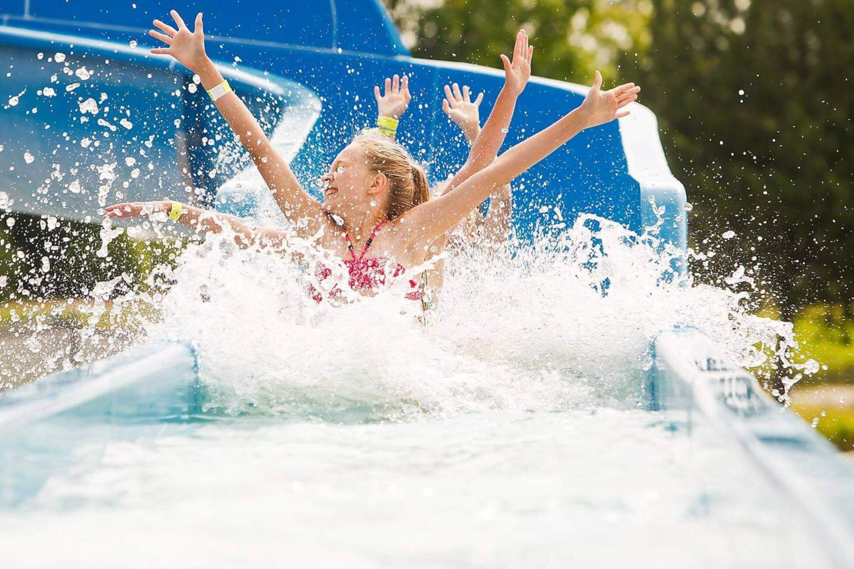 Une personne en maillot de bain éclabousse de l’eau en descendant un toboggan aquatique.