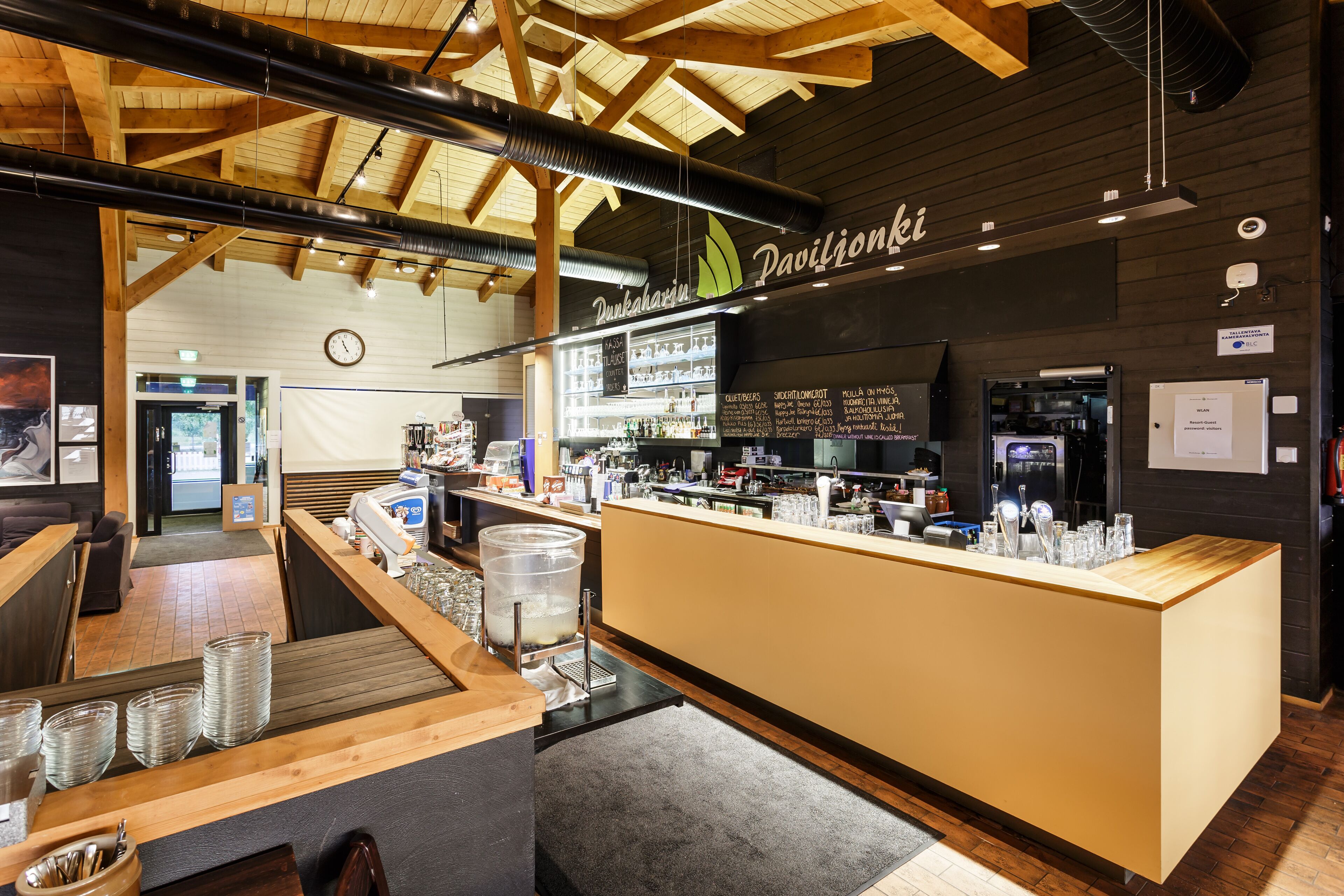 Een moderne bar met een houten plafond, een toonbank met drinkglazen en een menubord.