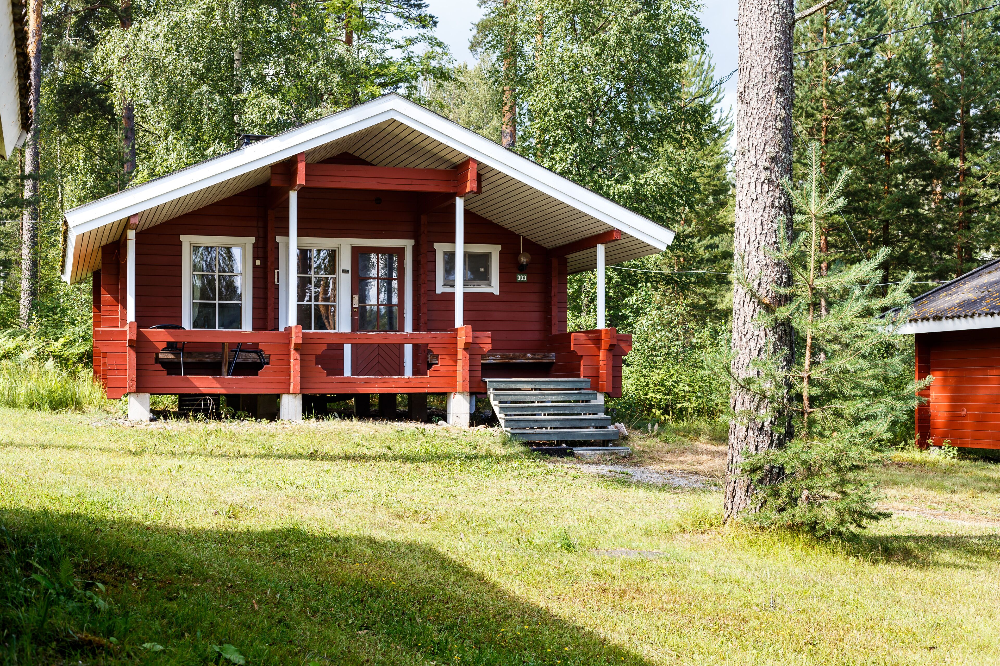 A red cabin with a porch and a chimney, surrounded by trees.