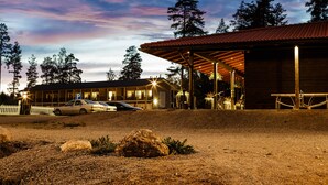 A building with a covered outdoor area, a parking lot with cars, and a natural landscape with trees. - Punkaharju Resort (Savonlinna)