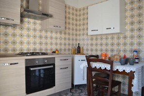 A kitchen with a stove, oven, and cabinets, a dining table with chairs, and patterned wallpaper.