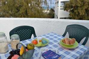 Una mesa con alimentos para el desayuno, un periódico y vistas al mar y edificios.