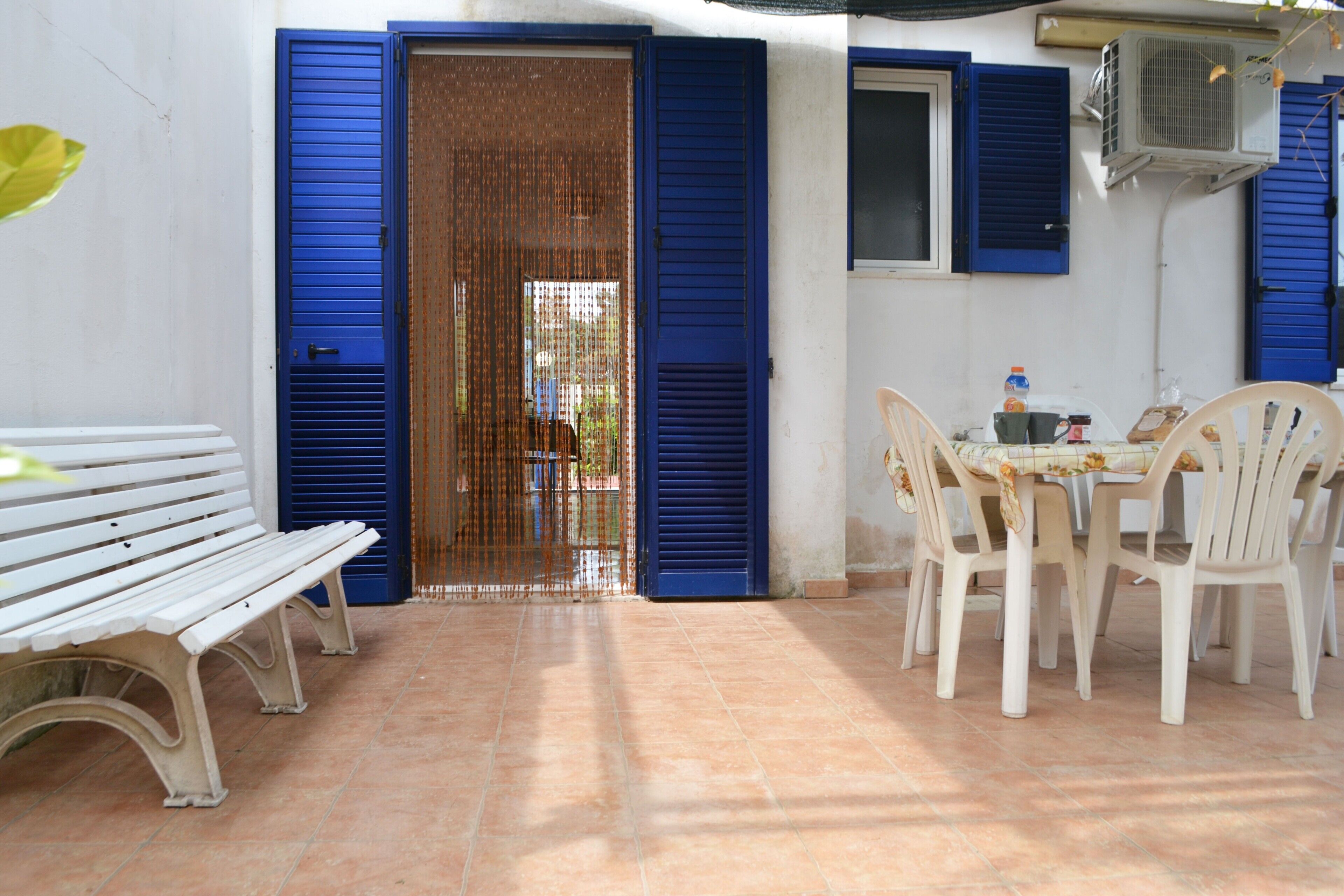 A patio with a white bench, a table with chairs, and blue shutters on the walls.
