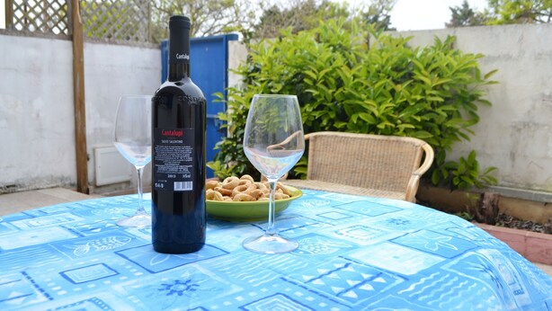 A bottle of Cantalupis wine, a glass, and a bowl of snacks on a table with a blue patterned tablecloth. - Charming Beachfront House with Spacious Terraces and Garden (san foca)