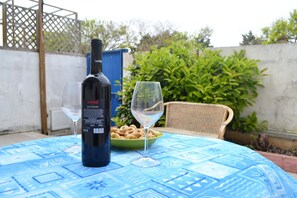 Een fles Cantalupis wijn, een glas en een schaal met snacks op een tafel met een blauwe tafelkleed.