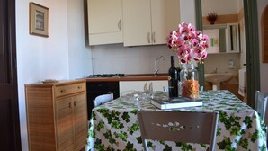 Uma cozinha com armários, uma mesa com toalha, uma cadeira, um vaso com flores e uma pia.