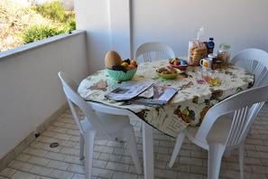 Une table à manger avec des chaises, un saladier de fruits, une bouteille et un verre.