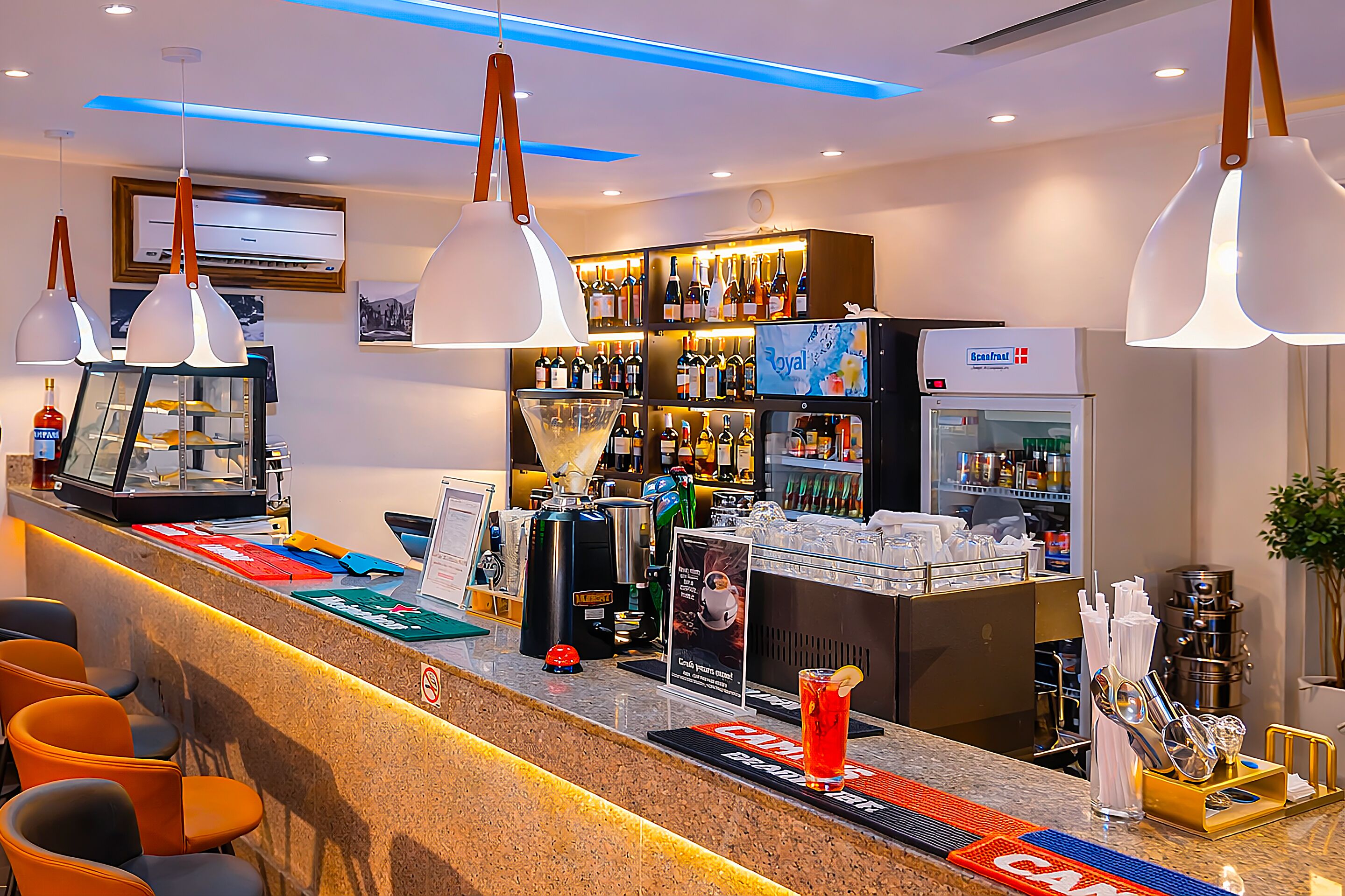 A bar area with a counter, bar stools, a refrigerator, and a shelf with bottles.