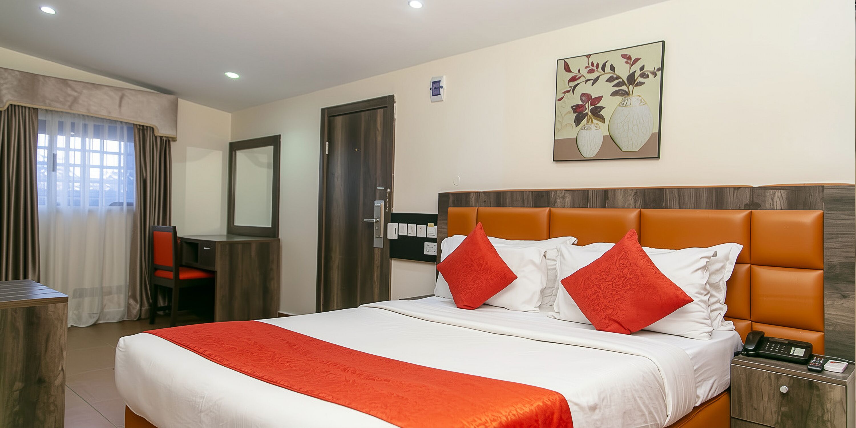 Ein Hotelzimmer mit Bett, Schreibtisch, Stuhl, Kleiderschrank und einem Gemälde an der Wand.