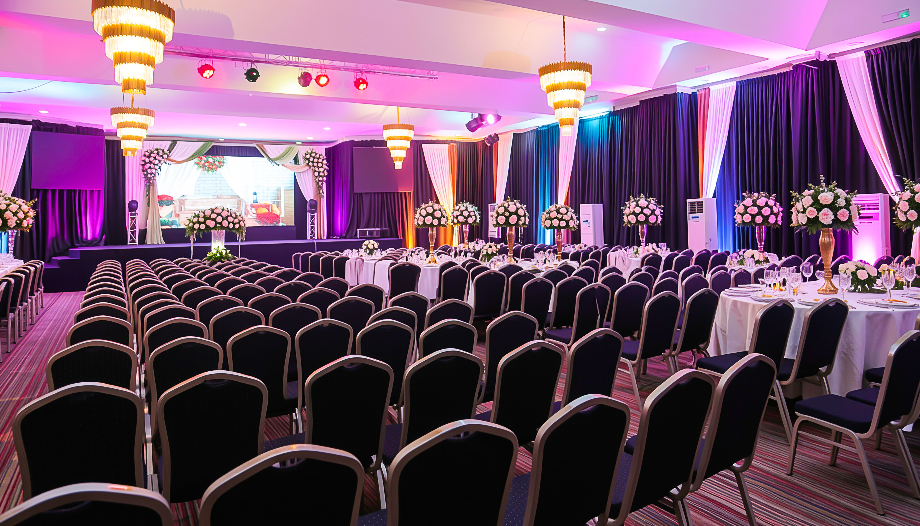 A banquet hall with rows of chairs, tables set for dining, and decorative floral arrangements.