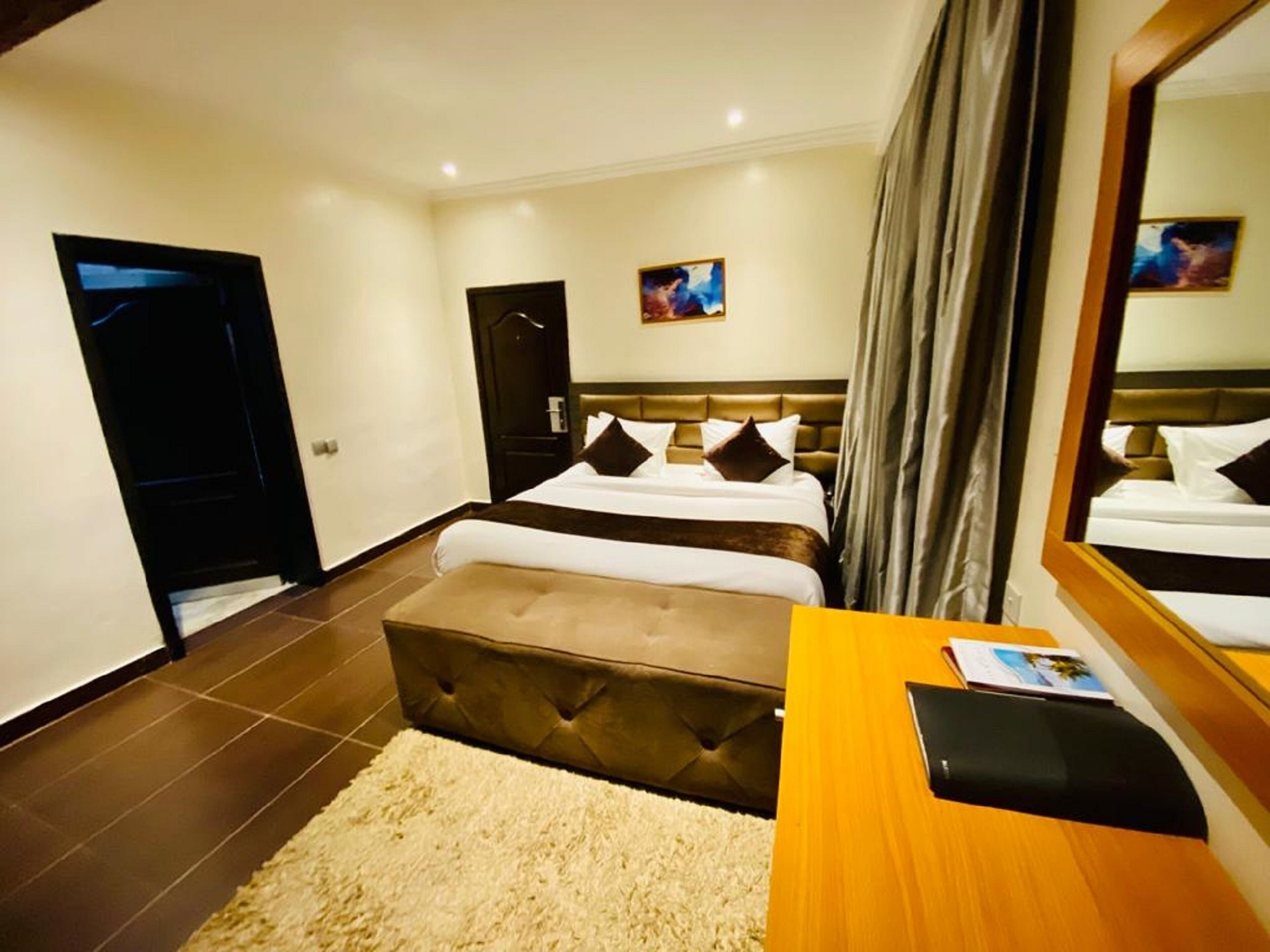 Une chambre d’hôtel avec un grand lit, un bureau en bois, un miroir et une porte.