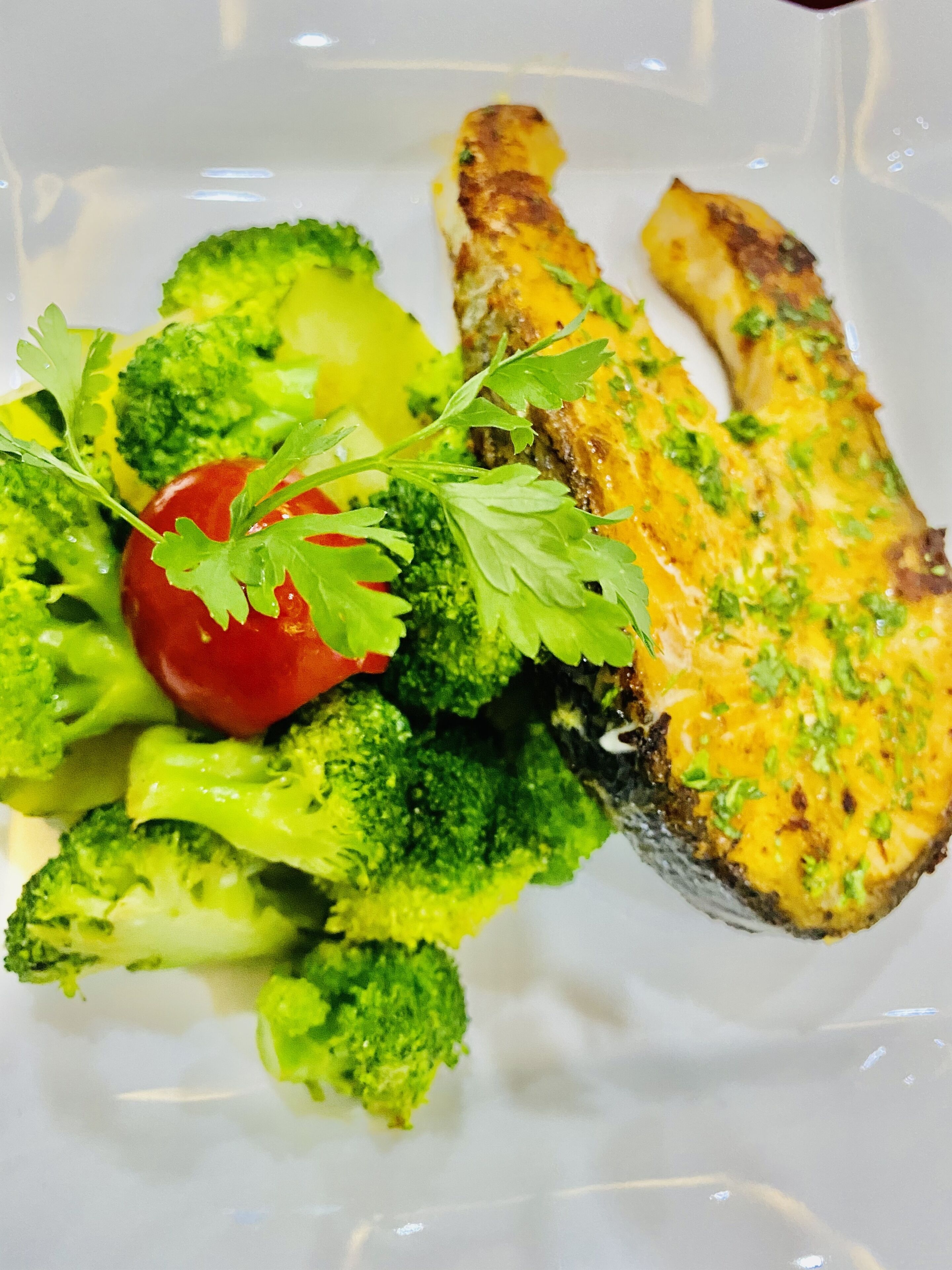 A plate with grilled chicken, broccoli, and a cherry tomato.