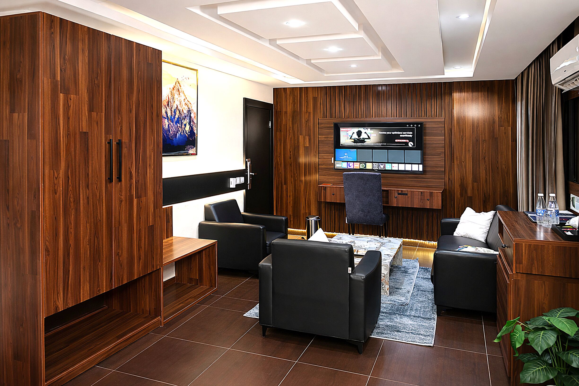 Una habitación de hotel moderna con un armario de madera, un televisor de pantalla plana, un sofá, una mesita de café y un pequeño escritorio con una silla.