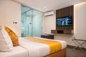 Habitación de hotel con cama, televisión, cabina de ducha de vidrio y panel de pared de madera.